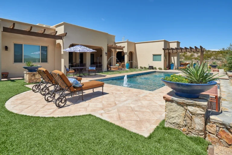 Desert backyard with a pool, pavers, stone planter columns and artificial turf in Las Cruces, NM